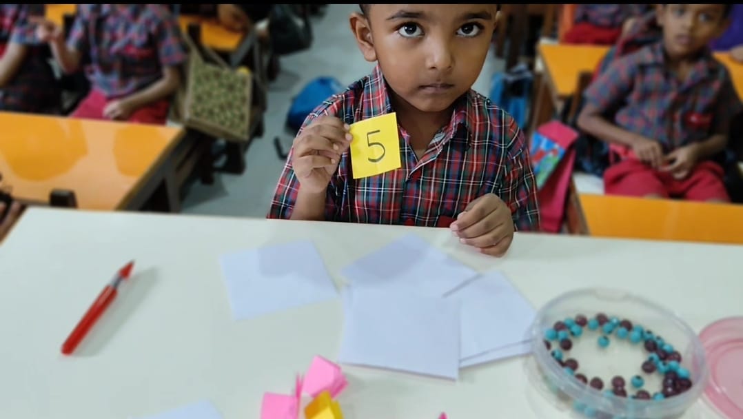 Child holding number card 5 next to beads bowl
